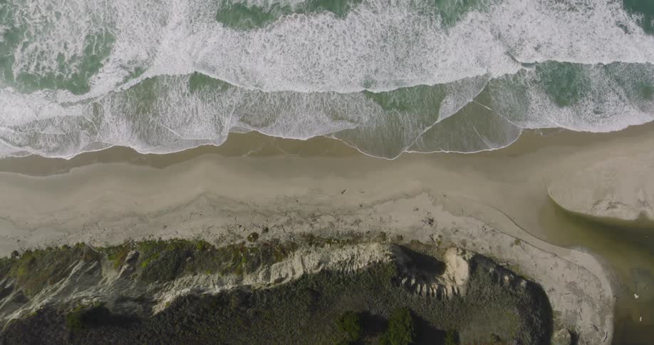 River flows into ocean across sandy beach near cliff