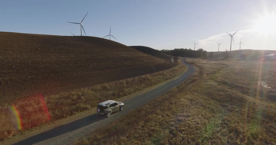 A van travels on a rural road around a curve through a wind farm
