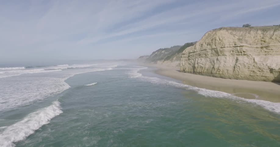 Waves roll onto beach at the base of cliff on a cloudy day