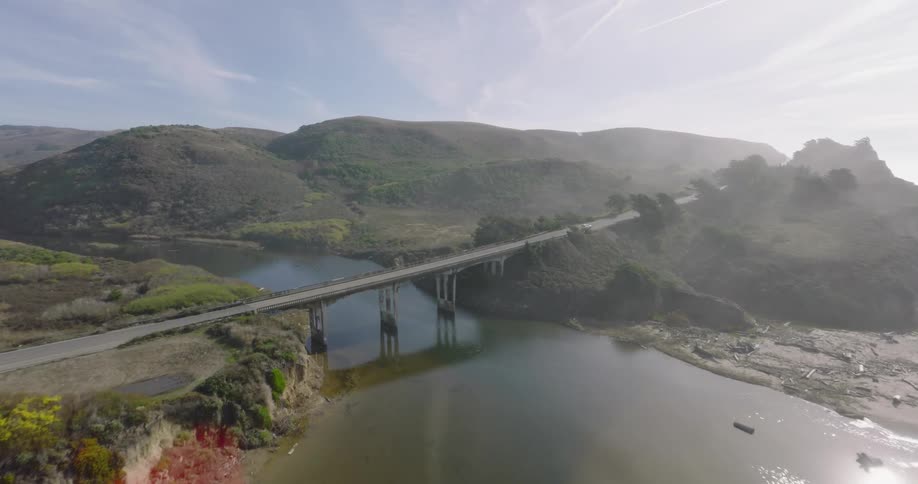 Vehicles cross bridge over river ending in a pond near the beach on a foggy day