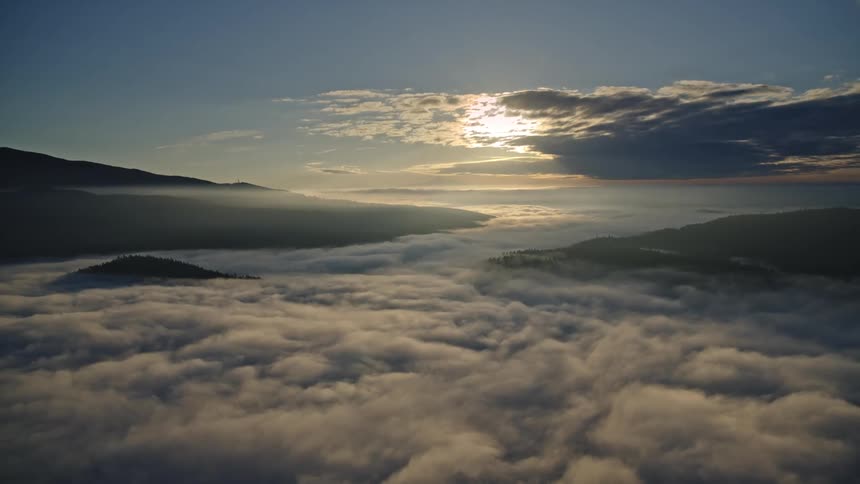 Expansive aerial view of mountain peaks shrouded in clouds at sunrise