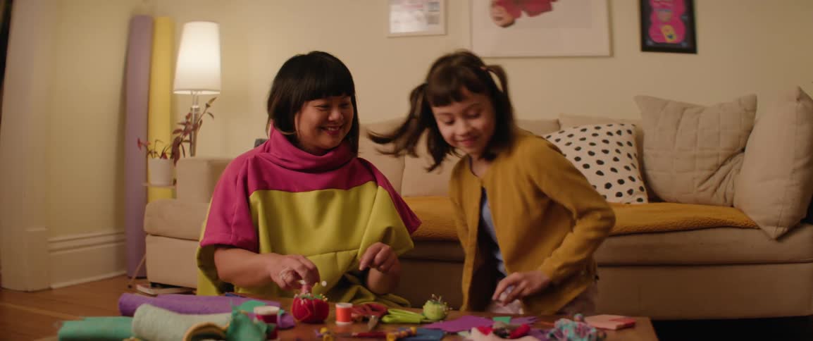 A daughter sitting next to her mother while she is sewing at a table in the living room