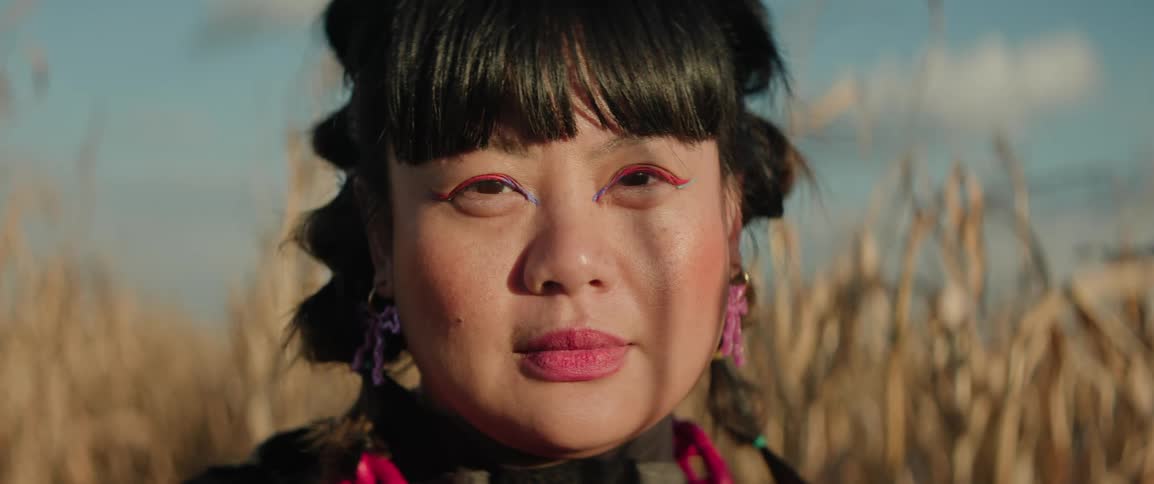 A portrait of a womans face looking at the camera with a corn field behind her