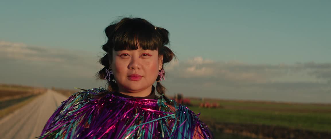 Portrait of a woman modeling in a shiny fashion outfit amidst a dirt road next to farm land