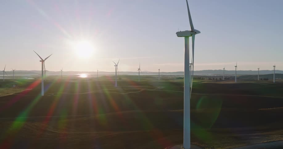 Panorama of a field with wind turbine platforms and engines in motion with the sun on the horizon