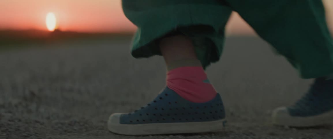 Closeup on the feet of a child jumping and twirling on the ground with the sunset on the horizon