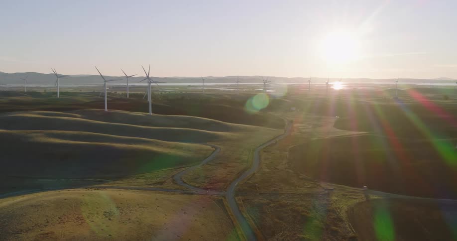 Panorama of a field with wind turbine platforms and engines in motion with the sun on the horizon