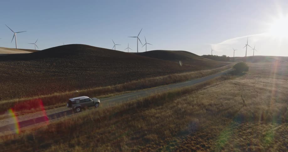 Car driving next to a grassland area with wind energy platforms