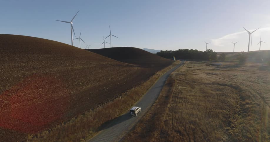 A car driving on a road at a wind farm on a sunny day