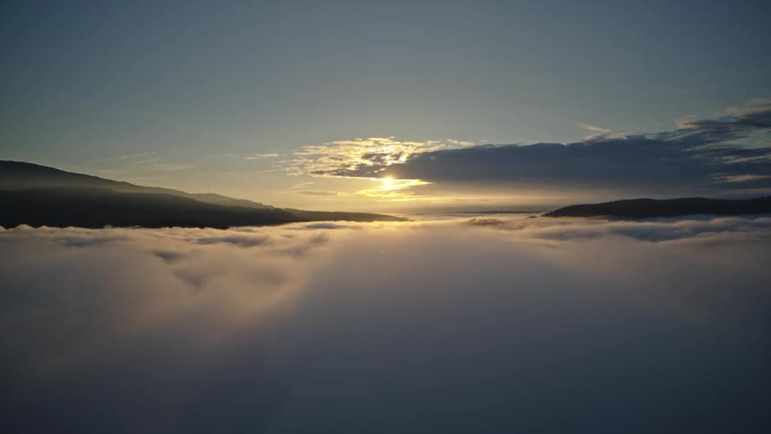 Aerial emerging from the clouds to reveal majestic sunrise over a foggy valley