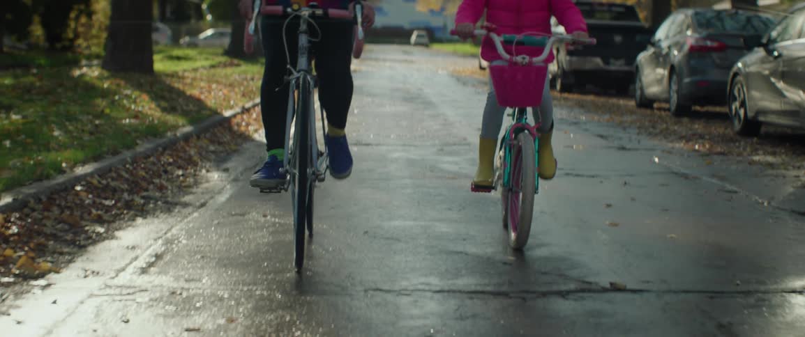 A woman and a young girl bicycling side by side on street