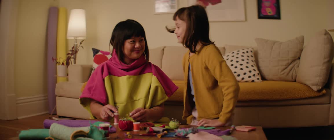Girl sitting next to her mother at a table filled with fabrics and linens
