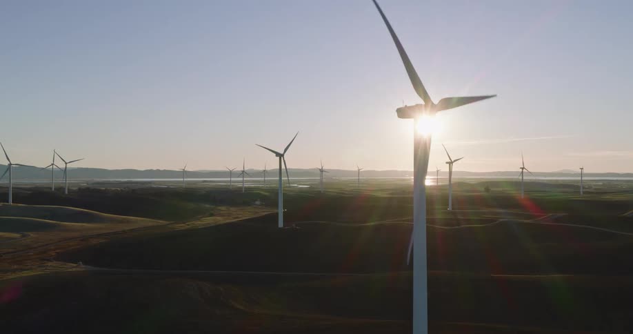 Wind turbines spin on a wind farm as the sun shines over mountains in the distance