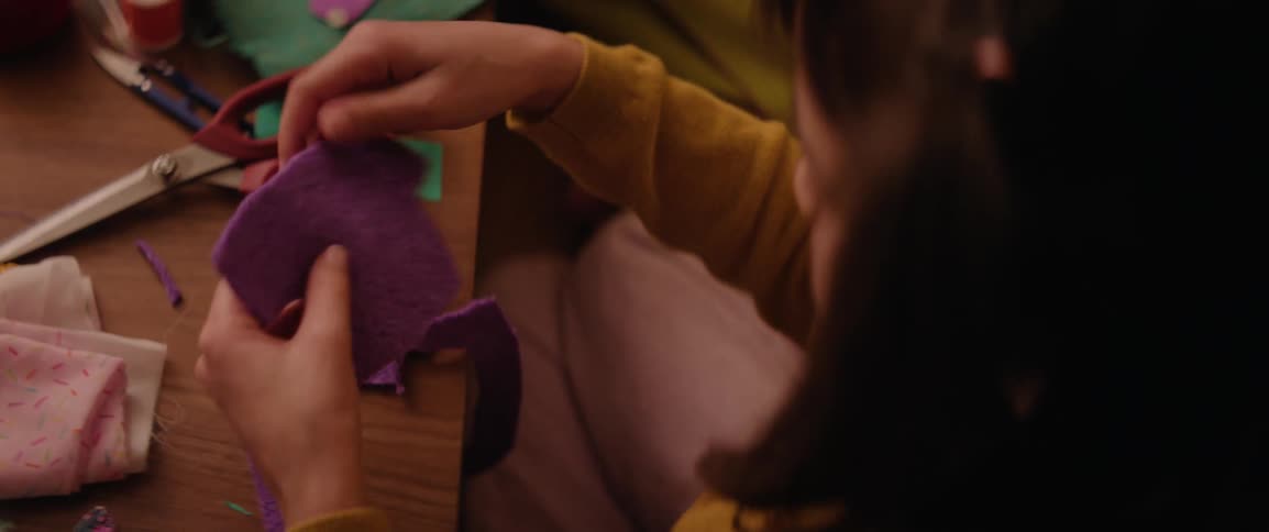 A girl and her mother sit at a table cutting out felt shapes from fabrics