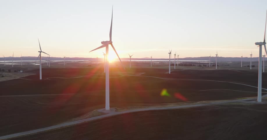 Wind turbines spin on a wind farm as the sun shines brightly on the horizon