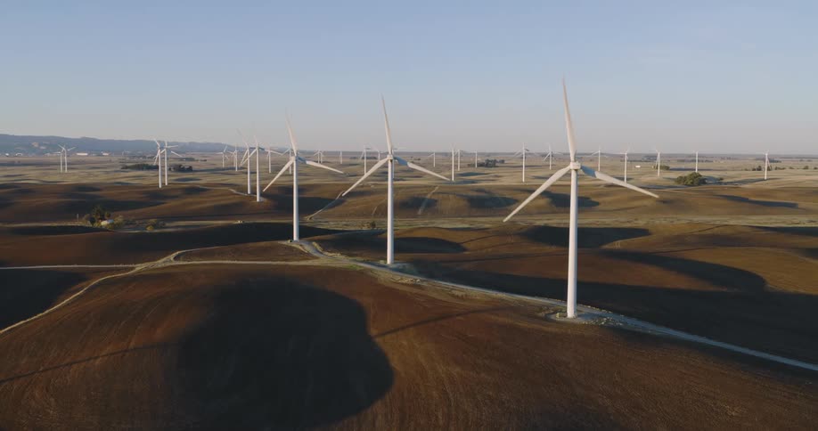 Wind turbines spin on a wind farm with mountains in the distance