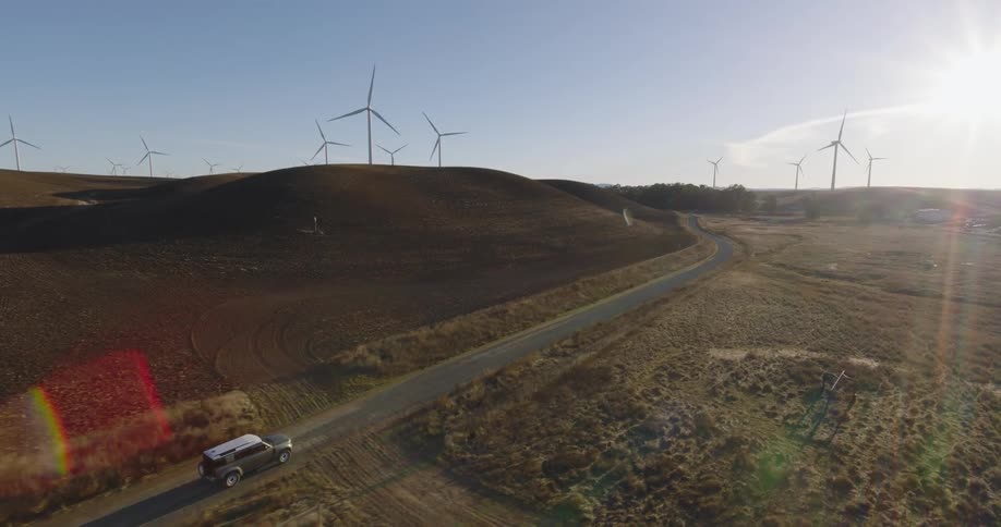 The vehicle drives past the windmills