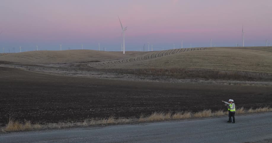 Two workers walking on the street next to a field with wind turbines on a day with a purple sky
