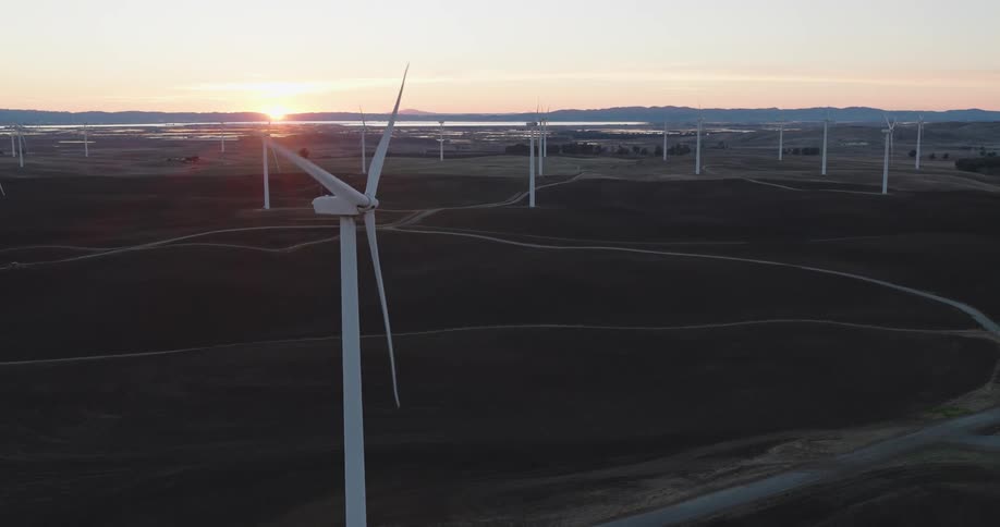 Several wind turbines are scattered around a vast grass covered field