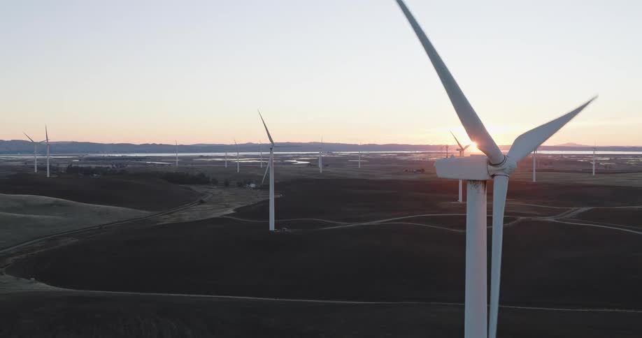 Panorama of wind energy turbines amidst fields with the sunset on the horizon