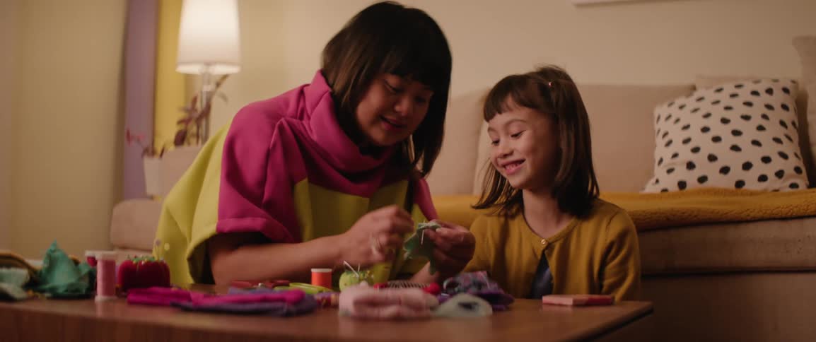 Woman sewing next to a girl who is watching and smiling