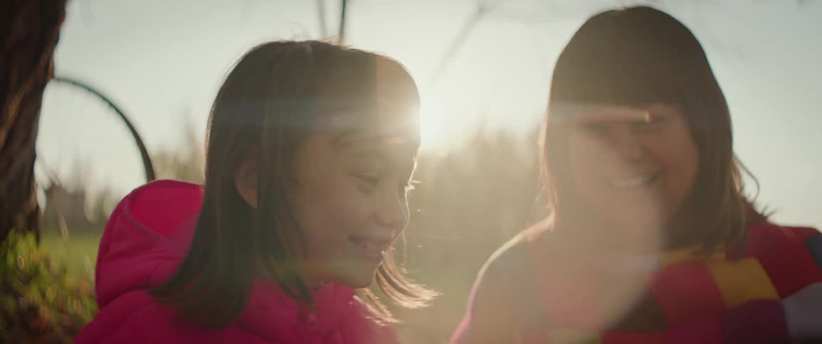 Mother and daughter laugh together at the base of tree on a sunny fall day