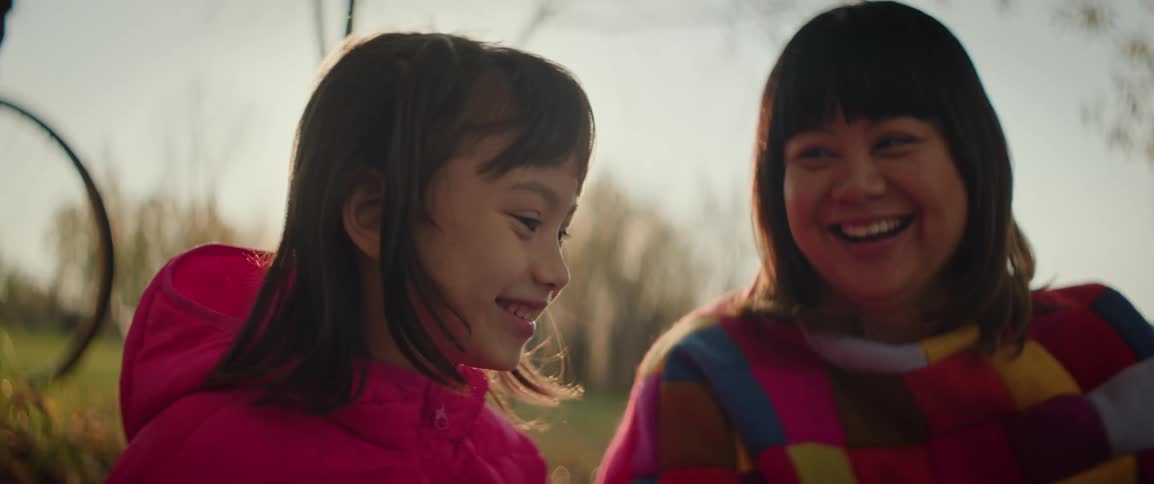 A woman and a girl smiling together in a park during sunset