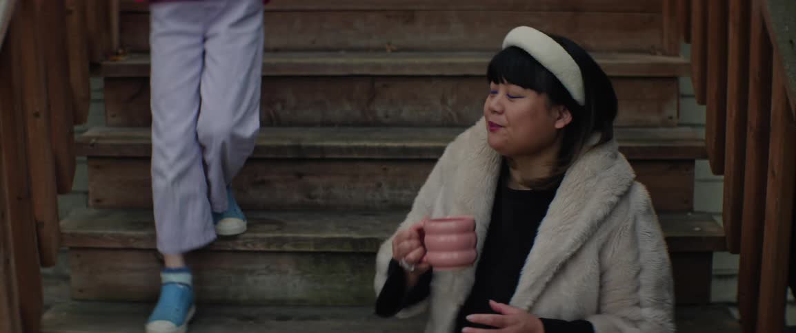 A mother and daughter sit on the stairs outside and drink from a mug