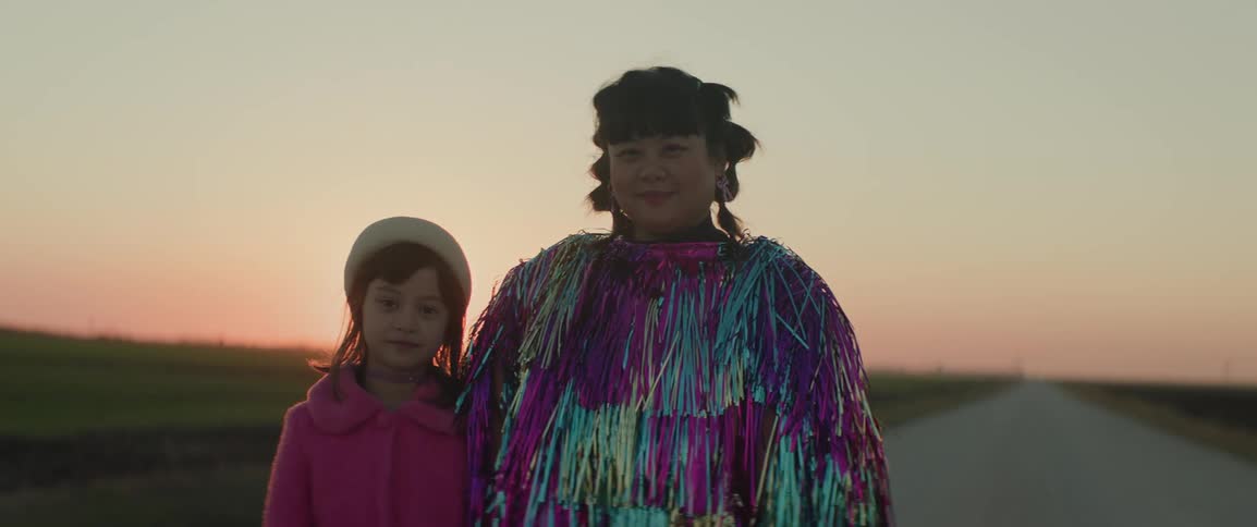 Mother next to her daughter in a pasture both wearing fashionable clothes with the sunset on the horizon