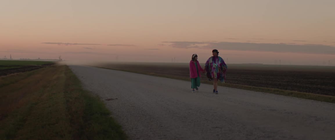 A woman and child walking down an empty dirt road in the soft evening light