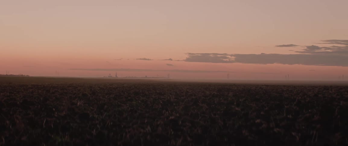 A large rural farm field under a red dusk sky