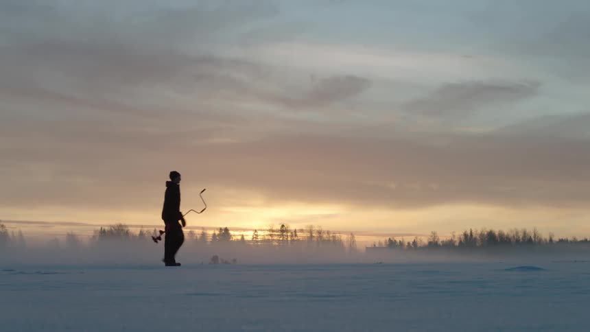 Person wearing winter clothes carries a tool across snow covered ground