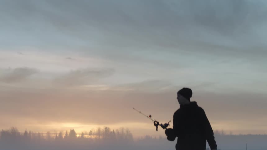 A man carrying fishing gear walks across a frozen lake at dawn