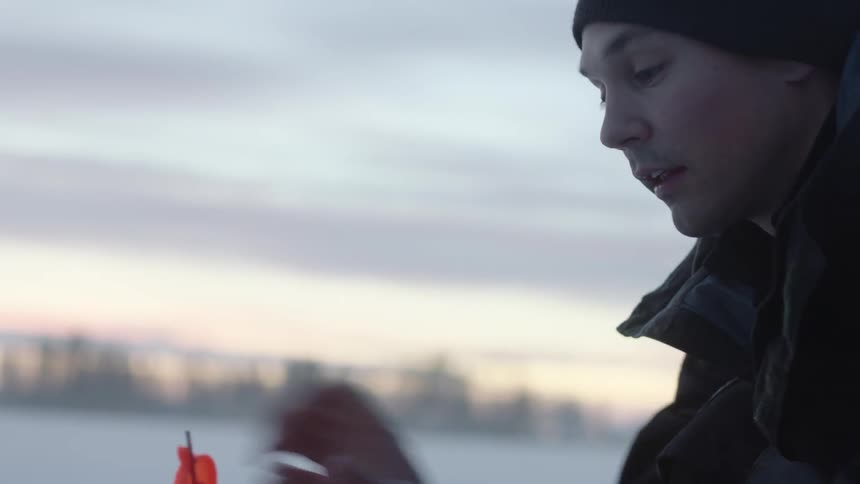 A man ice fishes at sunset