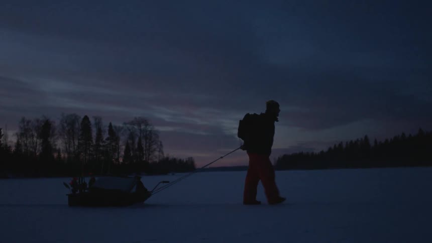 A person dragging a sled walks across the ice at dusk