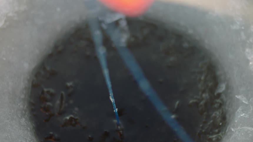 A fishing line is lowered into an ice hole