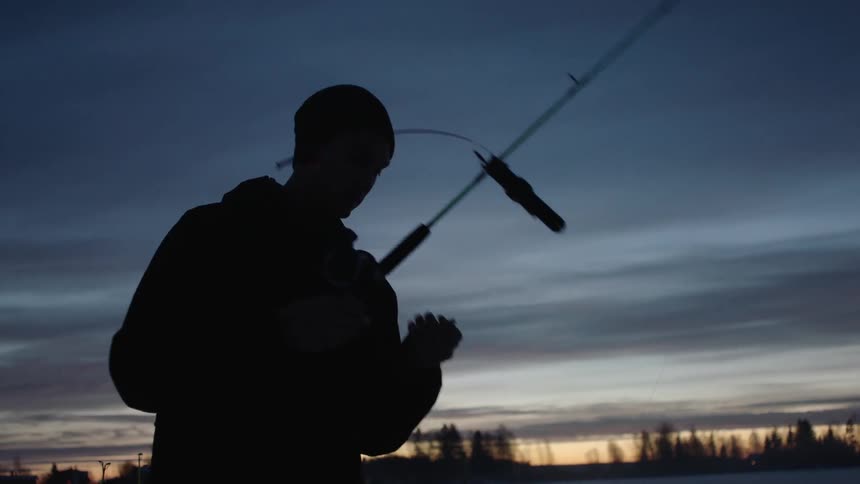 An ice fisherman adjusts his fishing line at dawn