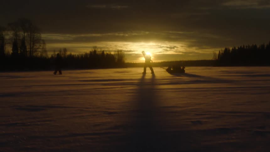 A person pulls a sled over snowy plains at sunset