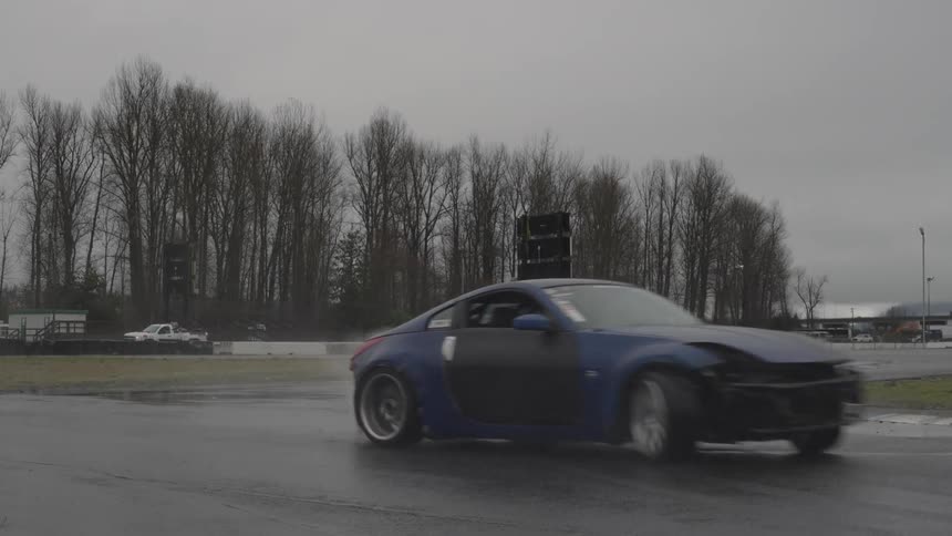 Cars race around track skidding through puddle on curve and splashing water