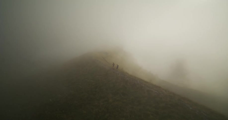 Two people walk along trail at top of ridge on a dense foggy day