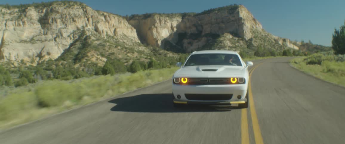 A white sports car travels on a road with mountains in the distance