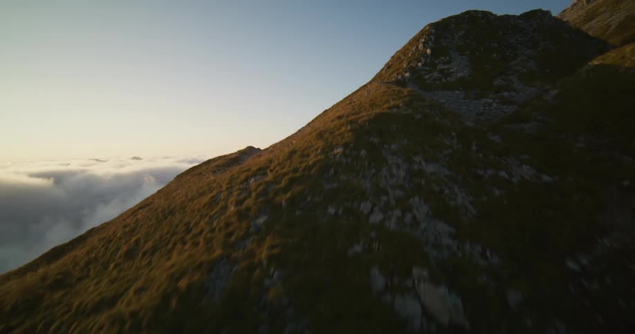 Aerial view of a grassy mountain side overlooking a fog bank