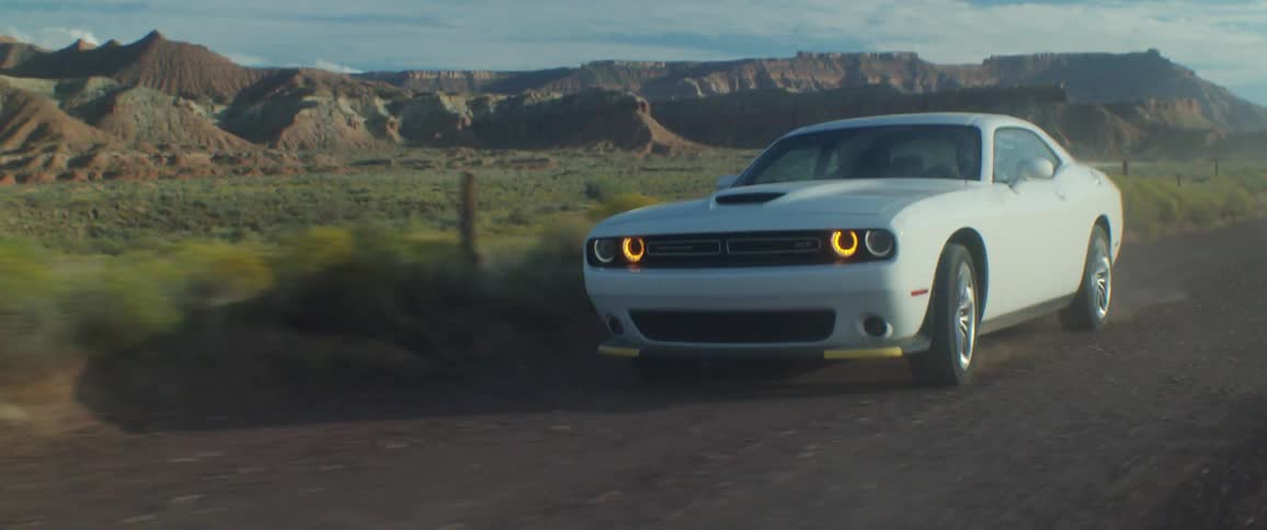White sports car drives on a dirt road on through the countryside
