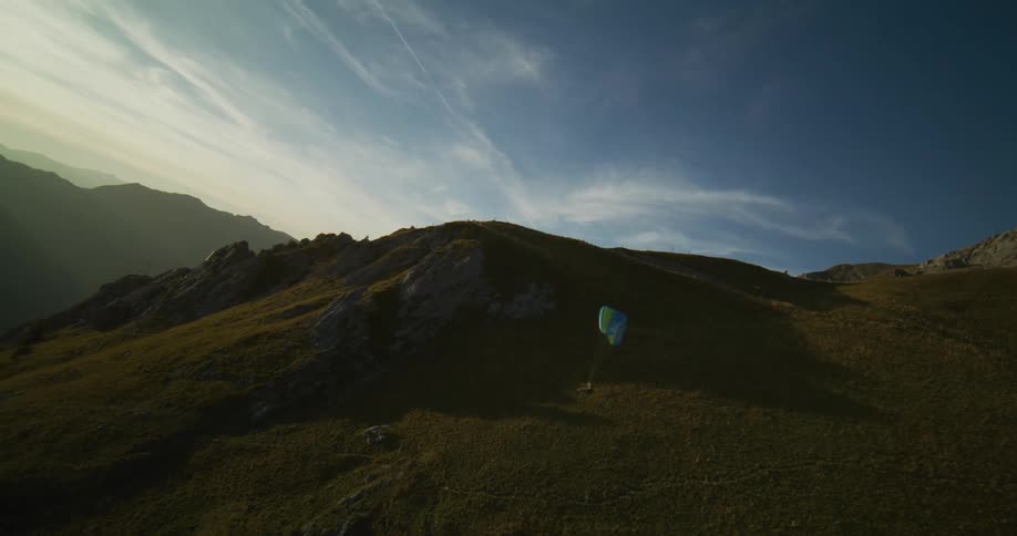 A man flying a paraglider floats along the side of a mountain cliff