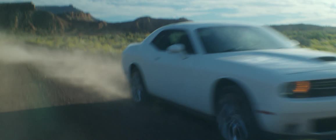 White sports car drives on a dirt road on through the countryside