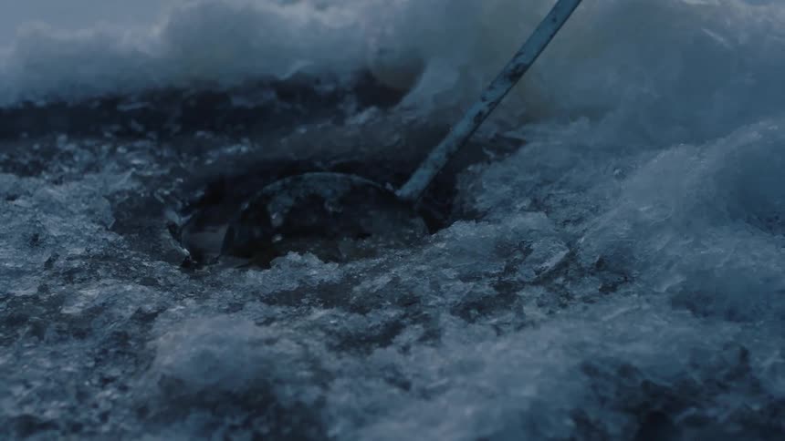 A person scoops the ice out of a fishing hole