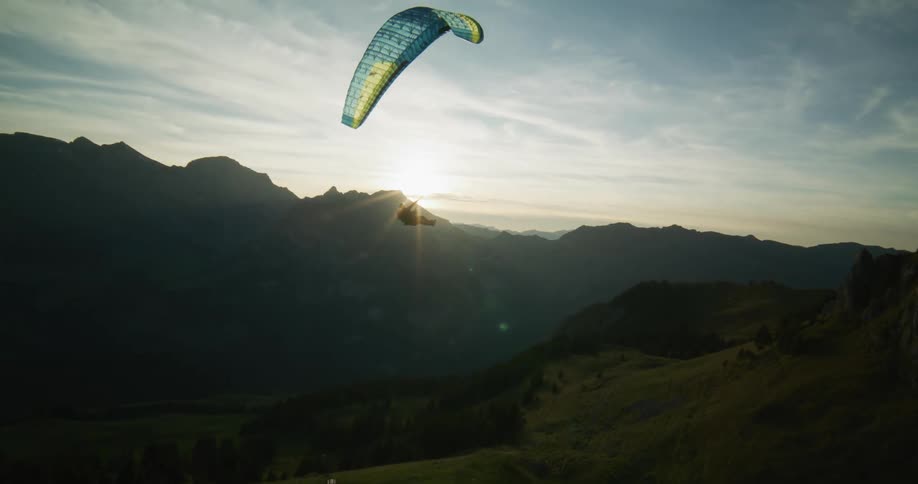 A man flying a paraglider floats over mountains