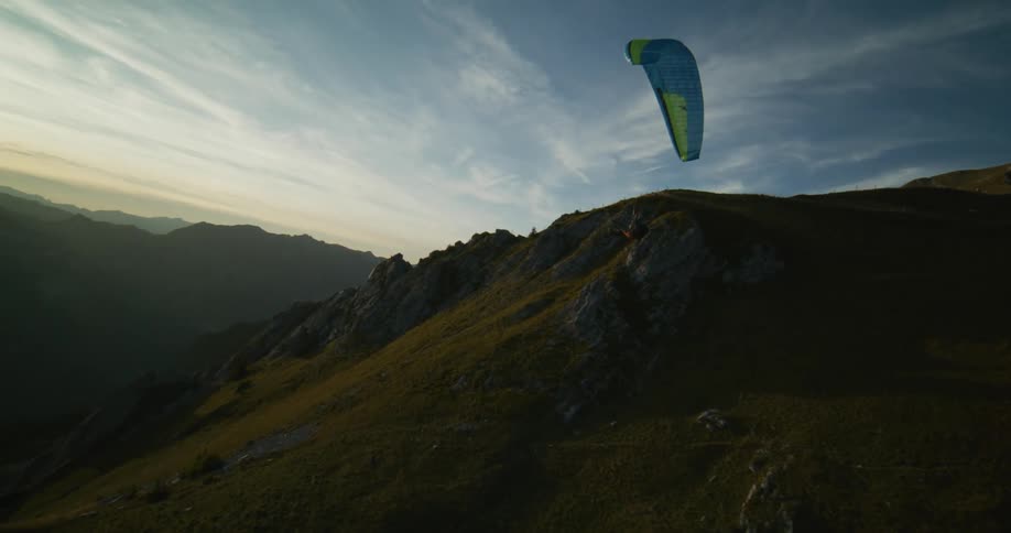 A man flying a paraglider floats over mountains