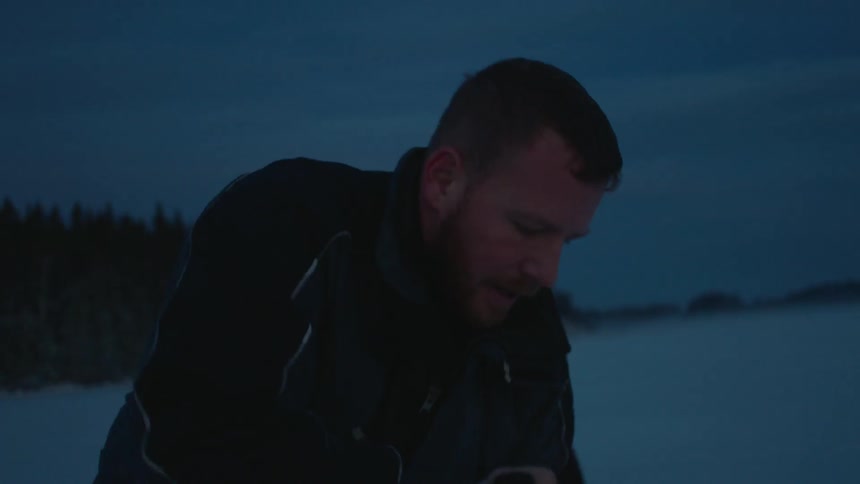 A man is using an ice auger to drill a hole in a frozen lake
