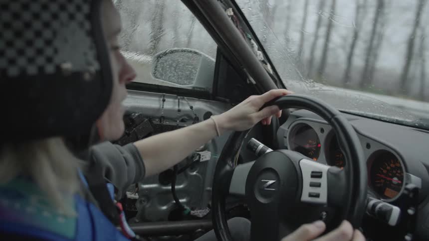 A woman wearing a helmet quickly driving a car and turning the steering wheel quickly